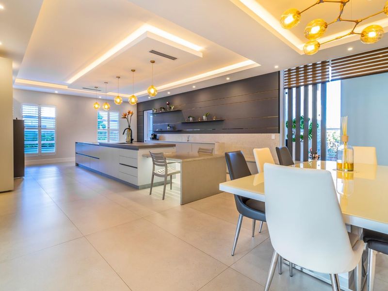 Modern open-plan kitchen and dining area featuring a large central island, recessed ceiling lighting, and high-quality tiled flooring throughout.
