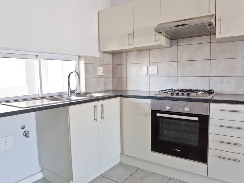 A clean, functional kitchen featuring built-in cabinetry, granite countertops, a gas hob, oven, extractor fan, and a stainless steel sink with tiled splashback.
