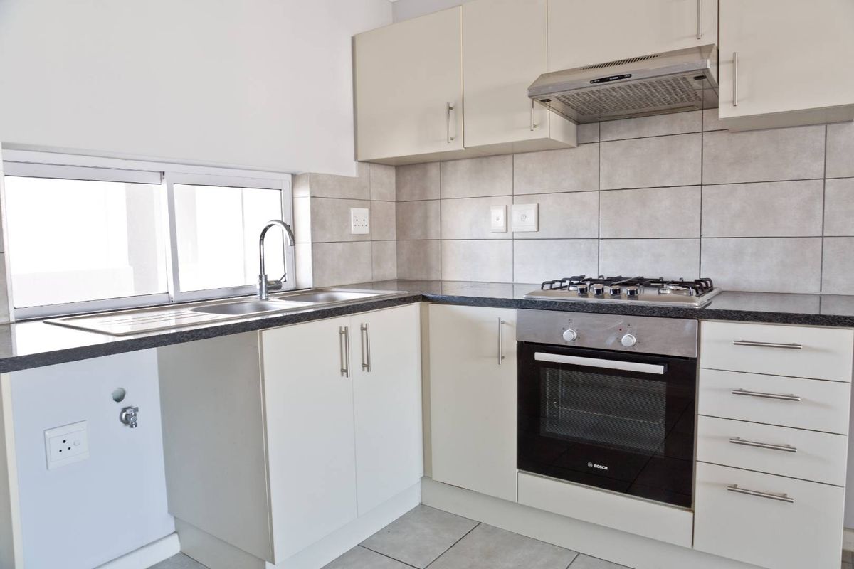 A clean, functional kitchen featuring built-in cabinetry, granite countertops, a gas hob, oven, extractor fan, and a stainless steel sink with tiled splashback.