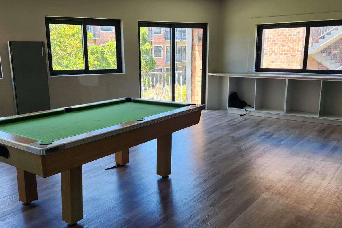 Spacious living area featuring wood-look flooring, large windows, and built-in shelving units, offering a versatile space for recreation or relaxation.