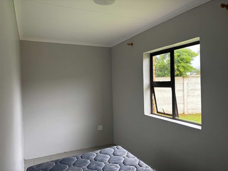 A simple, neutral-toned bedroom featuring tiled flooring and an aluminium-framed window, offering a clean and functional space ready for personalization.