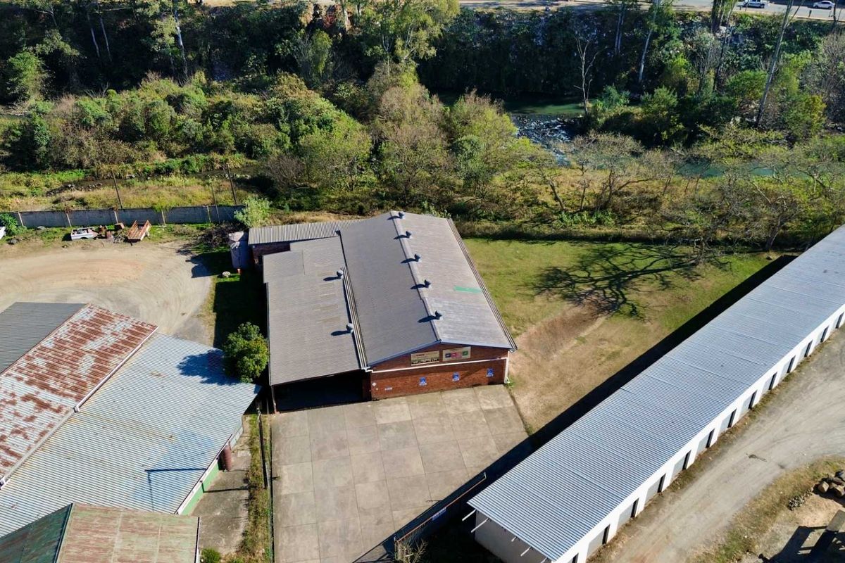 Aerial view of an industrial property featuring multiple storage buildings, a concrete yard, and a brick warehouse structure situated near a river.
