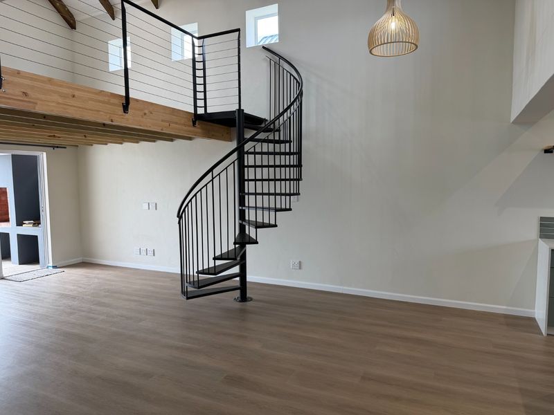 Spacious open-plan living area featuring a modern black spiral staircase leading to a mezzanine level with timber flooring and clean architectural lines.