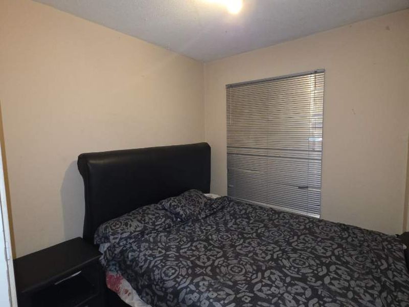 A compact bedroom featuring tiled flooring, venetian blinds, and a central ceiling light fixture, requiring minor cosmetic updates to the walls and ceiling.