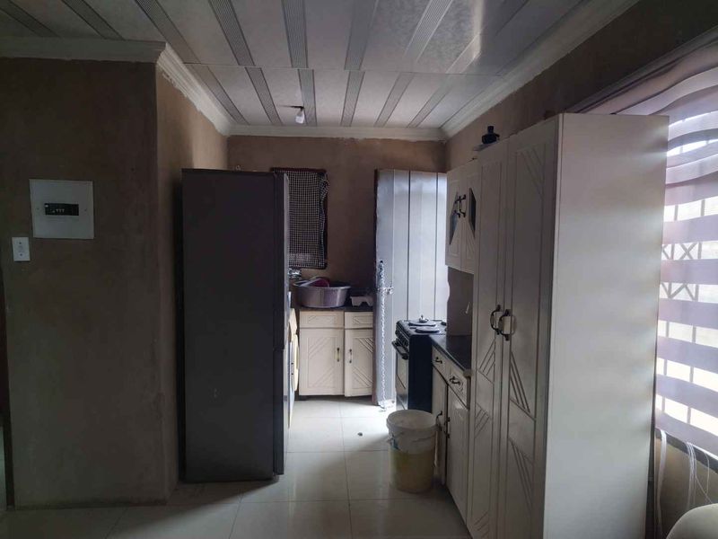 A functional kitchen space featuring built-in cabinetry, a stove, and tiled flooring, currently requiring cosmetic updates to wall finishes and cabinetry.