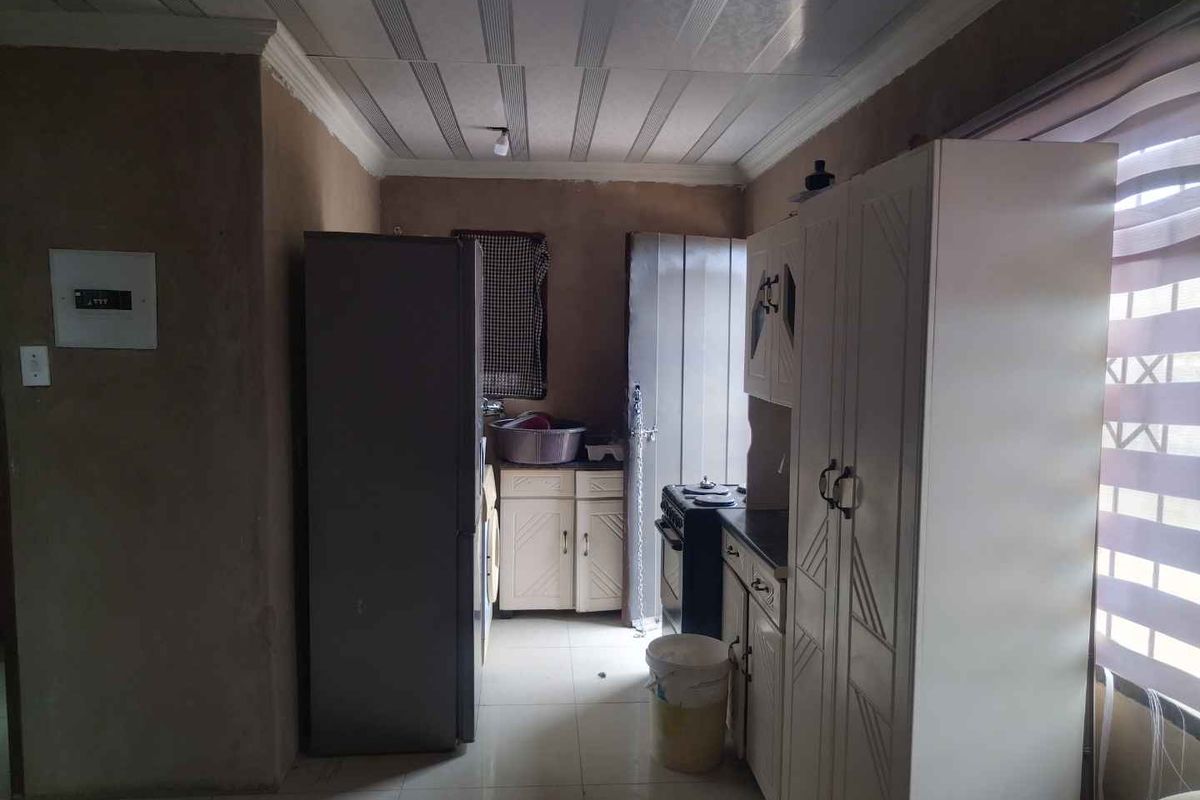 A functional kitchen space featuring built-in cabinetry, a stove, and tiled flooring, currently requiring cosmetic updates to wall finishes and cabinetry.