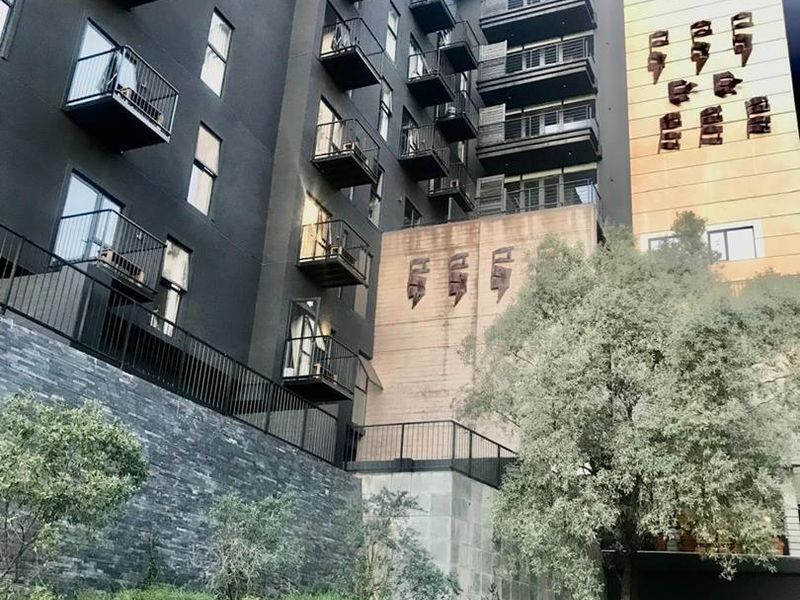 Modern apartment building facade featuring dark exterior finishes, multiple private balconies with metal railings, and stone-clad retaining walls with landscaped garden areas.