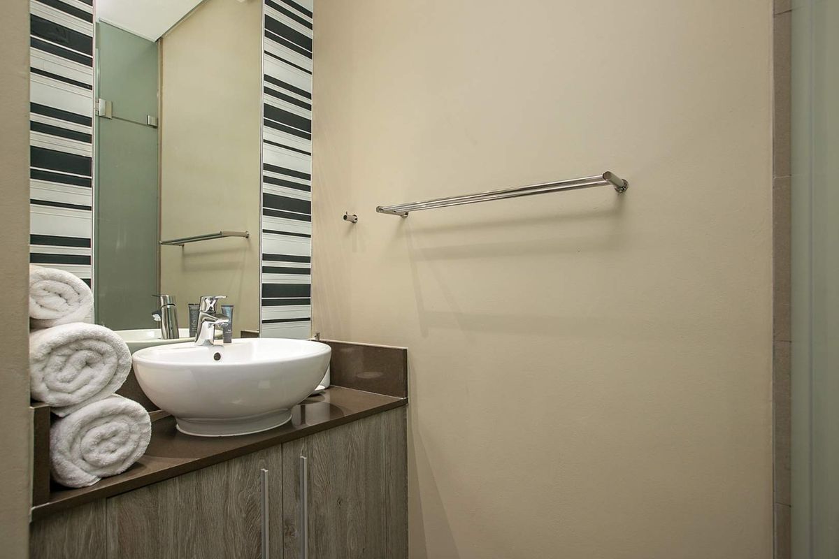 A modern bathroom featuring a vessel sink, vanity cabinet with stone countertop, large mirror, and a glass-enclosed shower area.