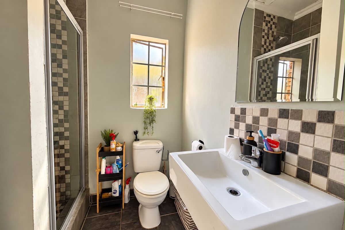 A functional bathroom featuring a shower enclosure, wall-mounted basin with tiled splashback, and a toilet, finished with neutral wall paint and tiled flooring.