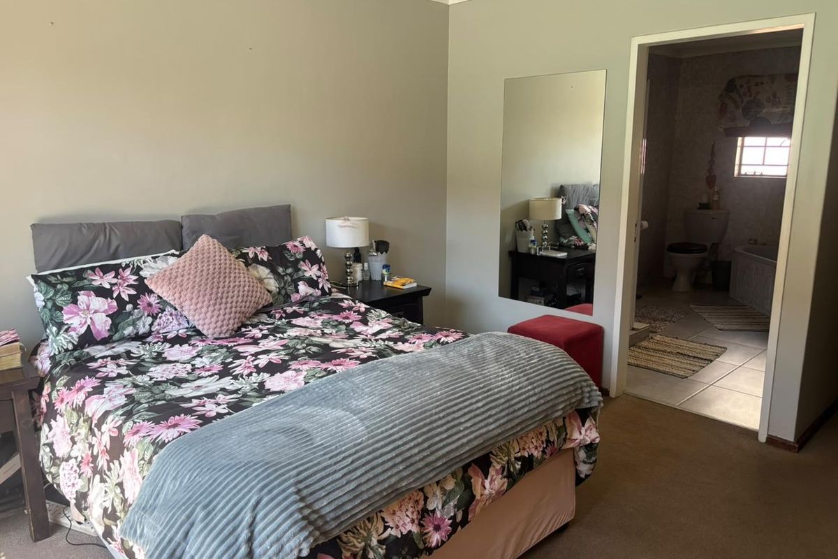 A bedroom featuring carpeted flooring and an adjoining en-suite bathroom with tiled floors and a wall-mounted mirror.