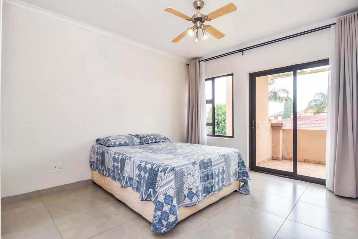 A bright bedroom featuring tiled flooring, a ceiling fan, and sliding glass doors that open onto a private balcony.