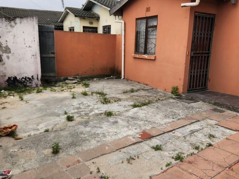 Rear exterior area featuring a paved patio, concrete yard, and boundary walls, requiring maintenance and landscaping to improve curb appeal.