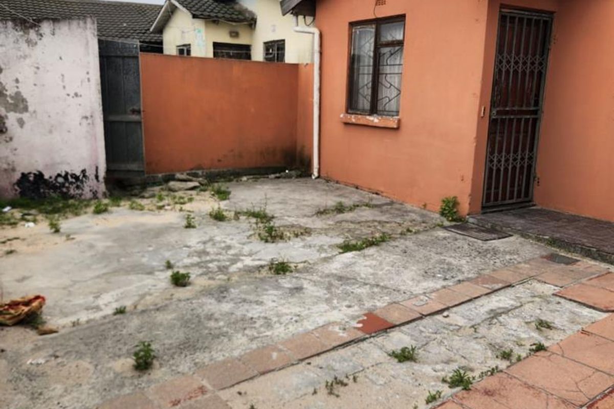 Rear exterior area featuring a paved patio, concrete yard, and boundary walls, requiring maintenance and landscaping to improve curb appeal.