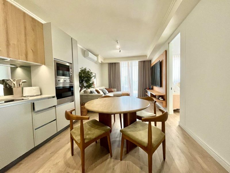 Modern open-plan living area featuring a sleek kitchen with integrated appliances, light wood-look flooring, and a seamless transition to the lounge space.