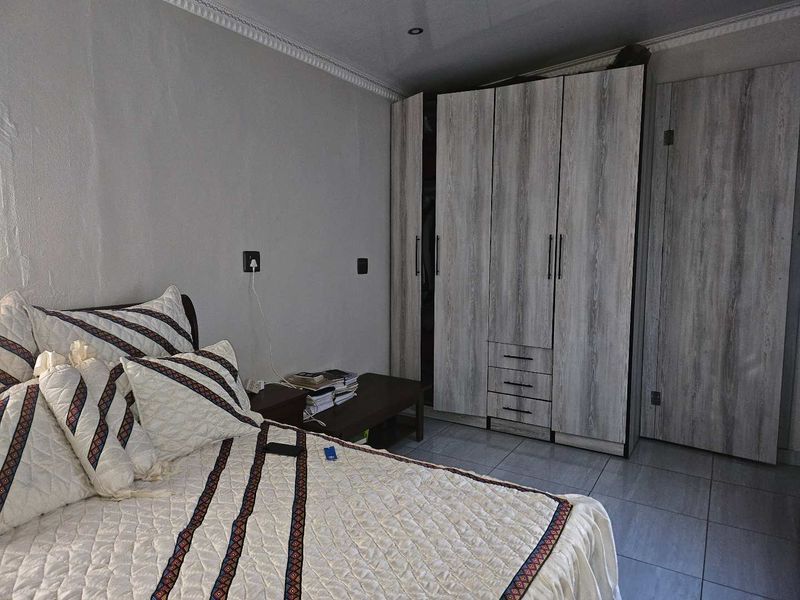 A bedroom featuring modern wood-look built-in cupboards, tiled flooring, and decorative ceiling cornicing.