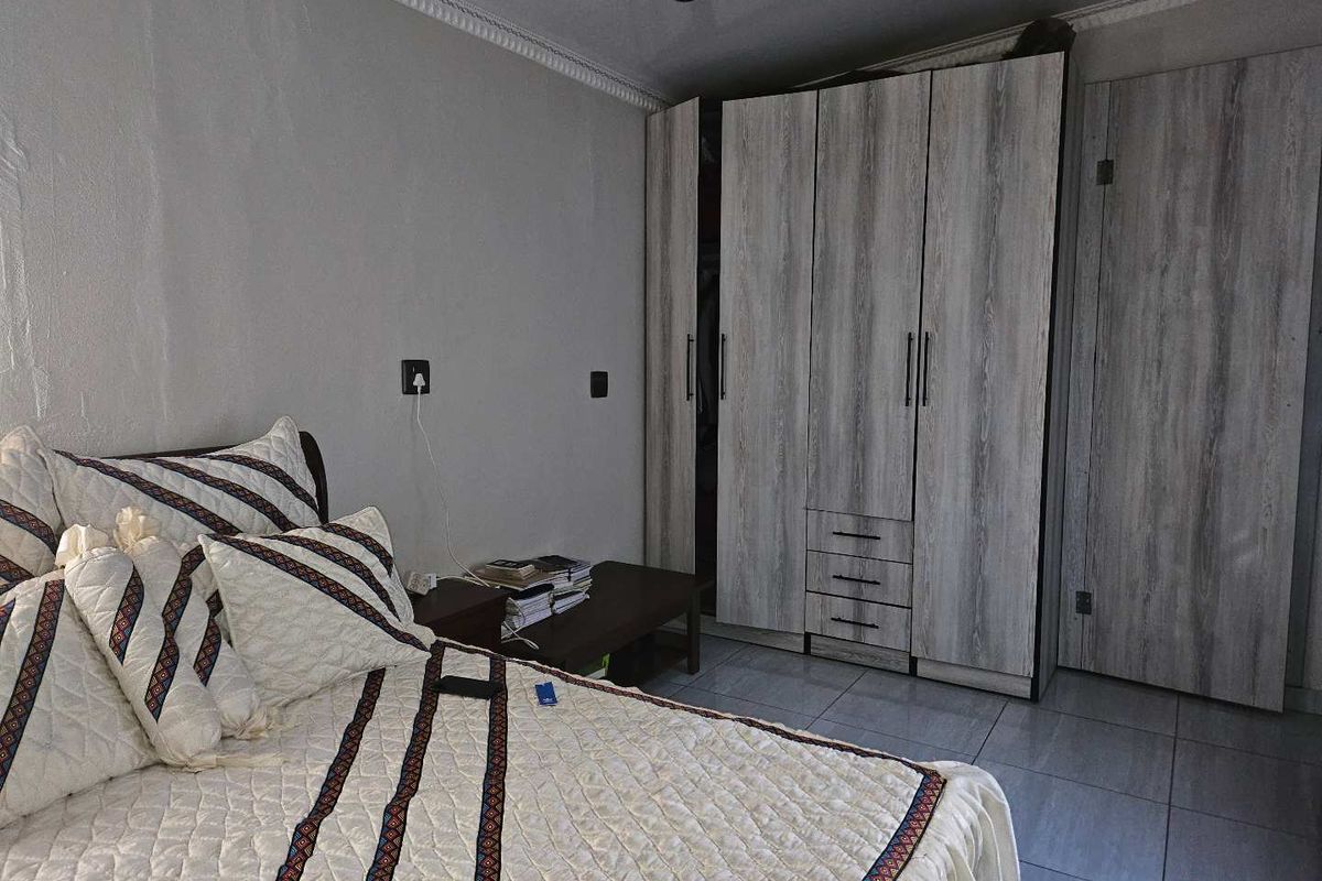 A bedroom featuring modern wood-look built-in cupboards, tiled flooring, and decorative ceiling cornicing.