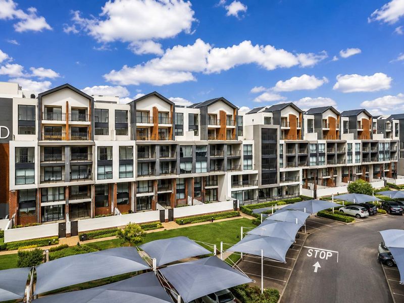 A modern multi-story apartment complex featuring private balconies, contemporary architectural design, landscaped grounds, and dedicated covered parking bays.