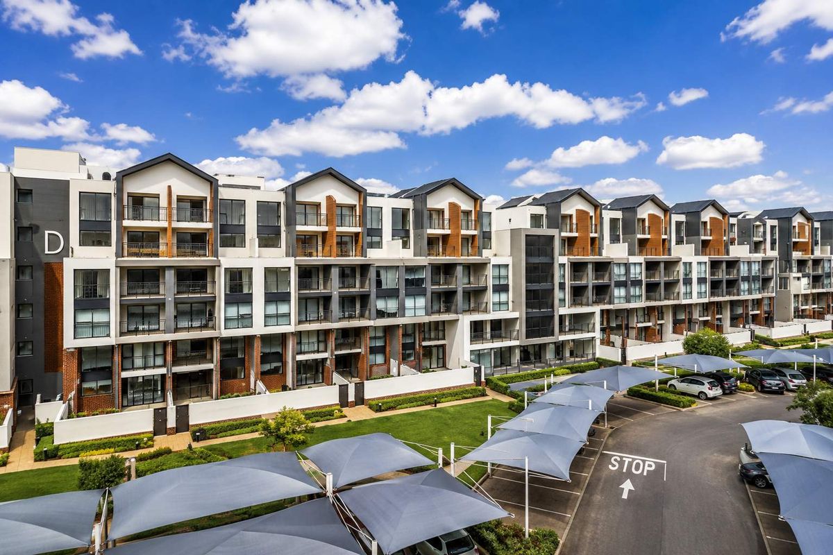 A modern multi-story apartment complex featuring private balconies, contemporary architectural design, landscaped grounds, and dedicated covered parking bays.