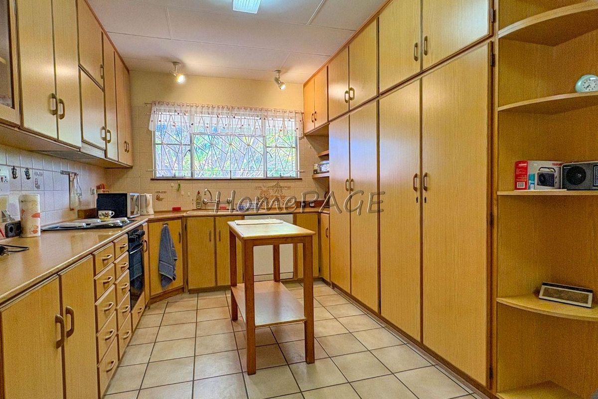 A functional kitchen featuring extensive built-in wooden cabinetry, tiled flooring, and a large window providing natural light.