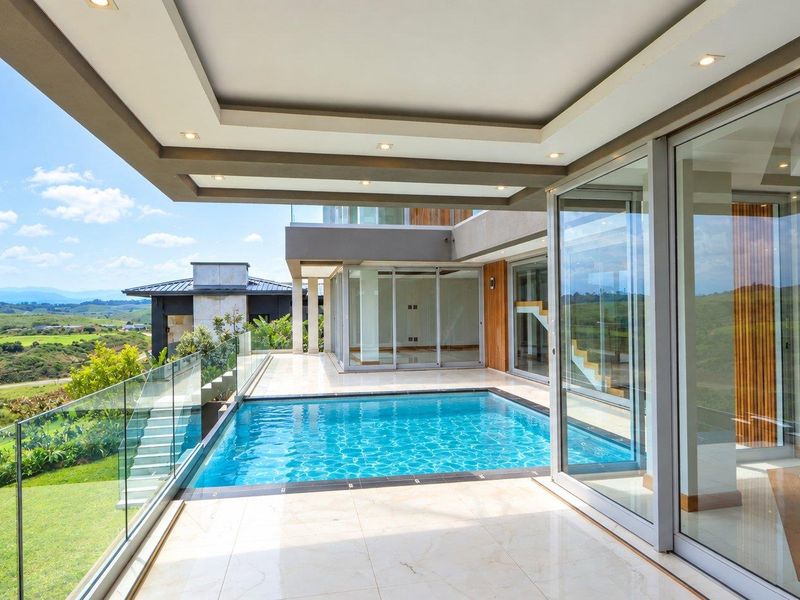 A modern outdoor pool area featuring a tiled patio, glass balustrades, and seamless access to the interior through large sliding glass doors.