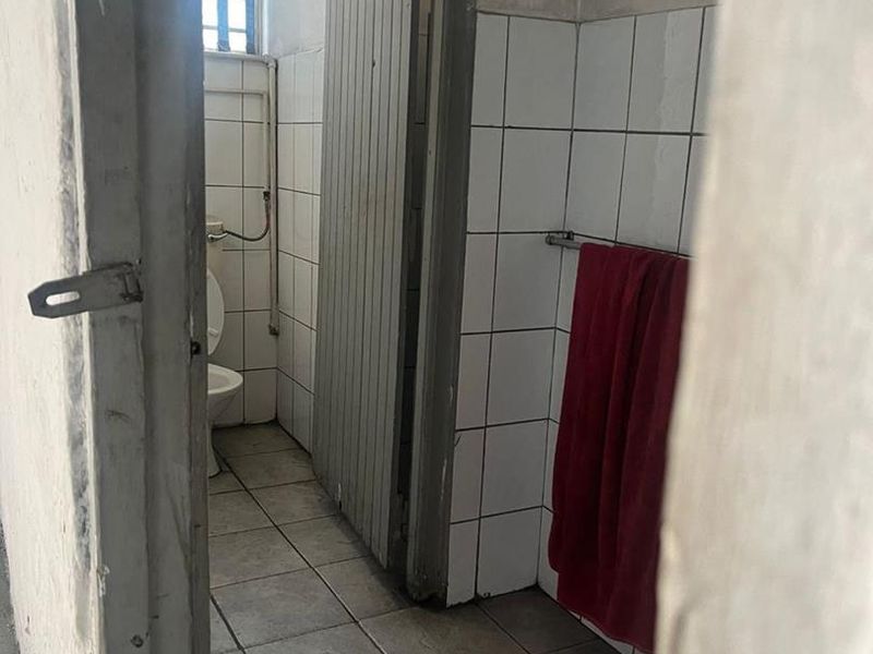 A small industrial-style bathroom featuring tiled walls and flooring, a standard toilet, and security bars on the window.