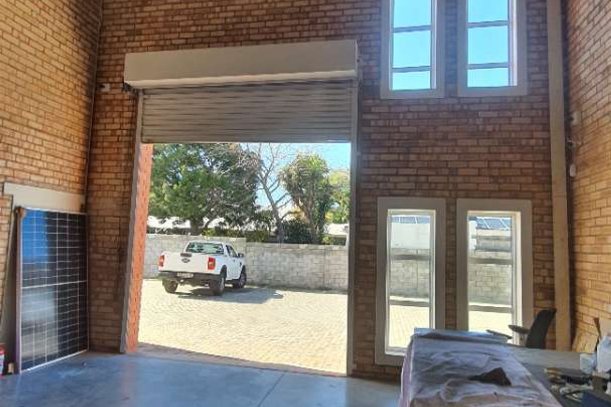 Spacious industrial utility area featuring high-volume ceilings, exposed brickwork, concrete flooring, and a large roller shutter door for easy access.