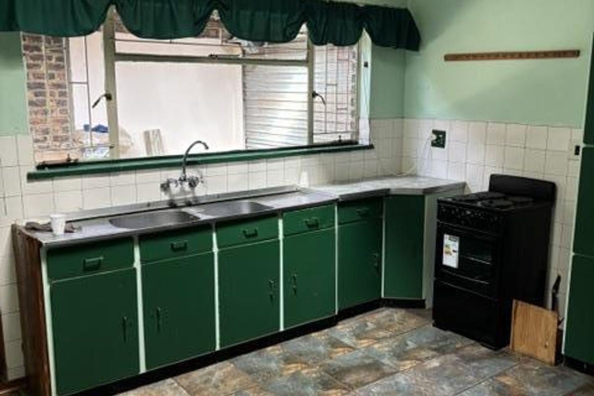 A dated kitchen featuring green cabinetry, a stainless steel sink, tiled splashbacks, and a freestanding stove, offering potential for a modern renovation.