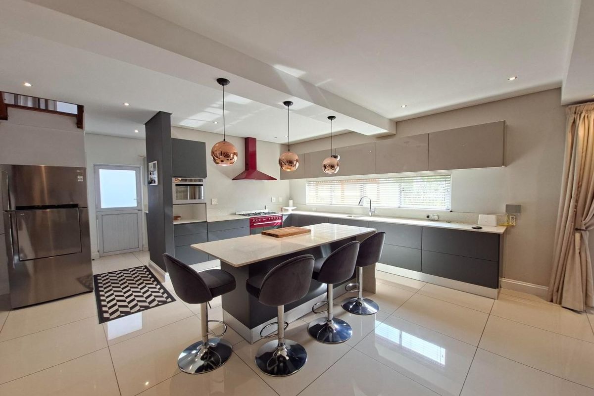 Modern kitchen featuring a central island with stone countertops, sleek grey cabinetry, high-end appliances, and polished tiled flooring in an open-plan layout.