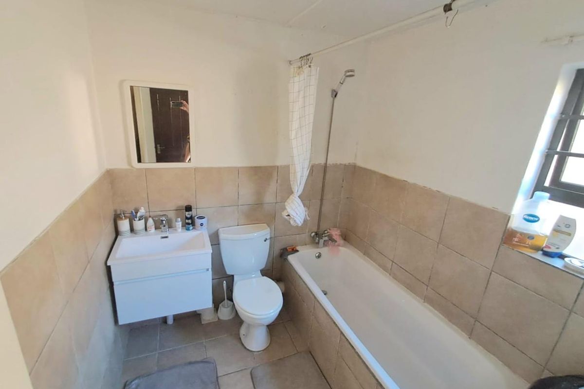 A functional bathroom featuring a bathtub with shower attachment, a wall-mounted vanity basin, and a standard toilet with neutral wall tiling.