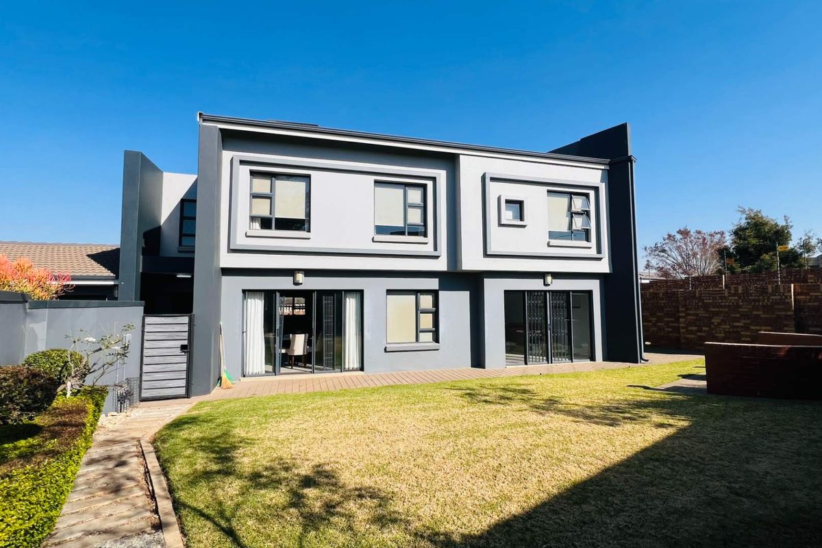 Rear view of a modern two-story house featuring a landscaped garden, wooden decking, and large sliding doors providing access to the interior.