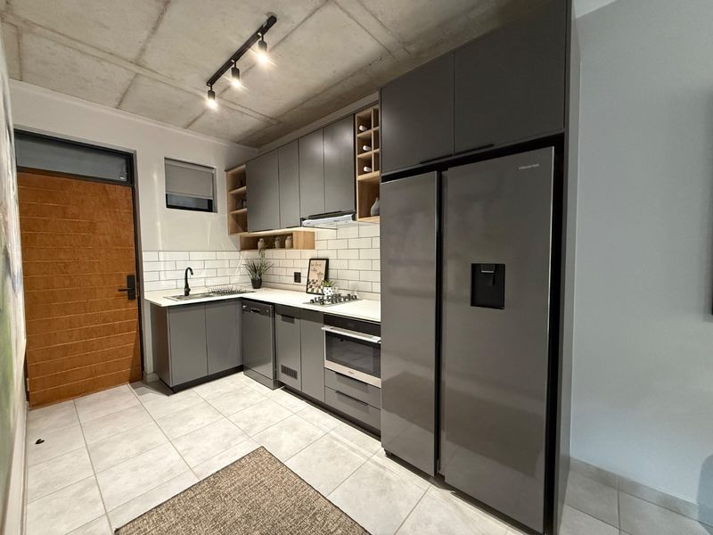 Modern kitchen featuring sleek grey cabinetry, subway tile backsplash, built-in appliances, and an industrial-style exposed concrete ceiling with track lighting.