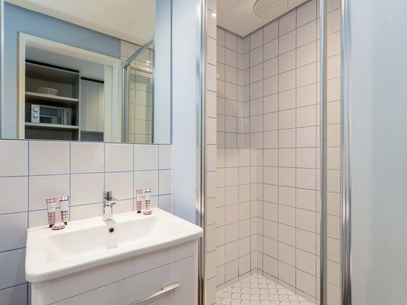 A clean, functional bathroom featuring a modern vanity, wall-mounted mirror, and a tiled shower enclosure with a rainfall shower head.