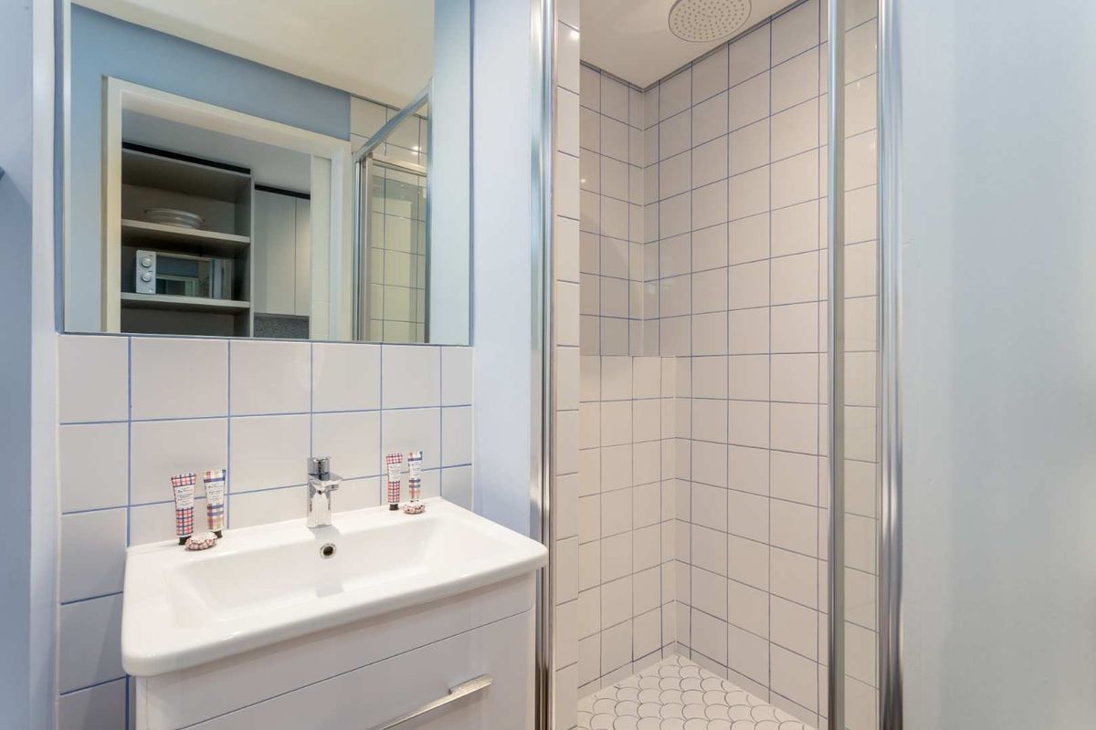 A clean, functional bathroom featuring a modern vanity, wall-mounted mirror, and a tiled shower enclosure with a rainfall shower head.