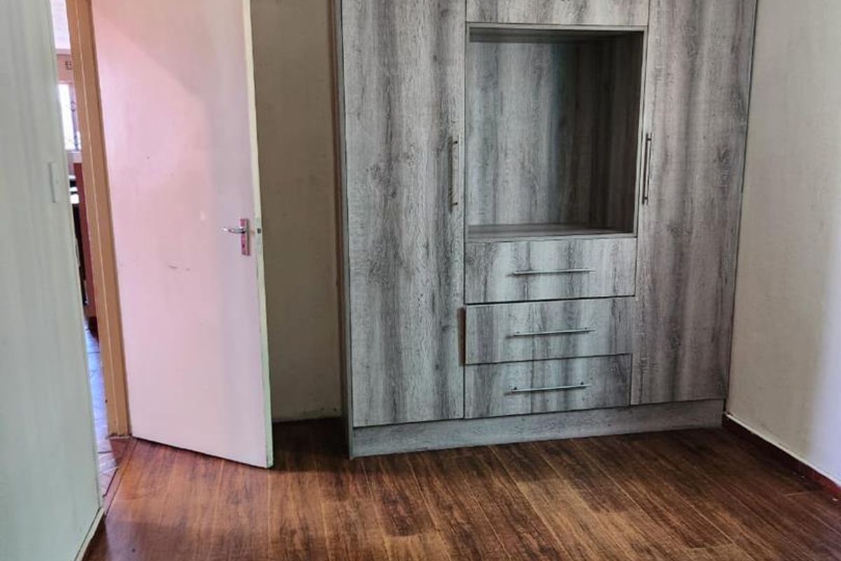 A bedroom featuring dark wood-look laminate flooring and a built-in wardrobe with integrated shelving and drawers.