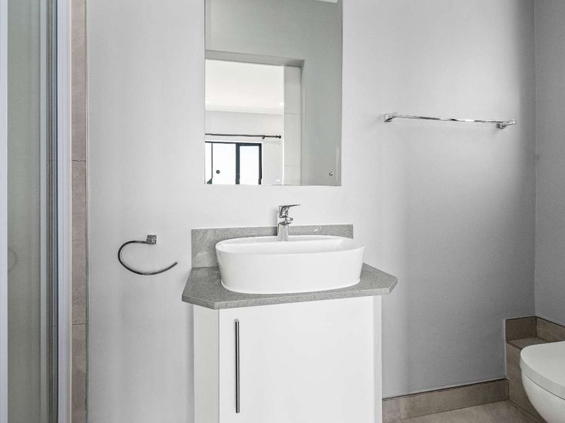 A clean, modern bathroom featuring a vessel sink vanity, wall-mounted mirror, toilet, and a glass-enclosed shower with neutral tiled finishes.