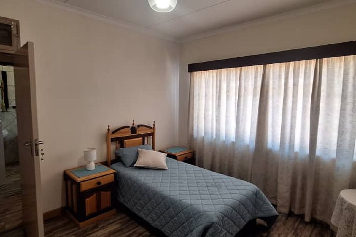 A well-maintained bedroom featuring laminate flooring, a large window with a pelmet, and direct access to an adjoining room.