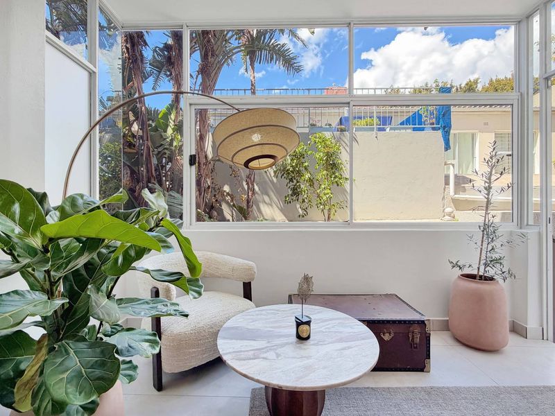 A bright and airy enclosed balcony or sunroom featuring large glass windows, tiled flooring, and a pleasant outlook onto the surrounding garden area.