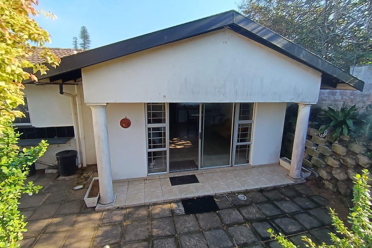 Rear exterior view featuring a covered tiled patio, sliding glass doors, and a stone retaining wall in a garden setting.