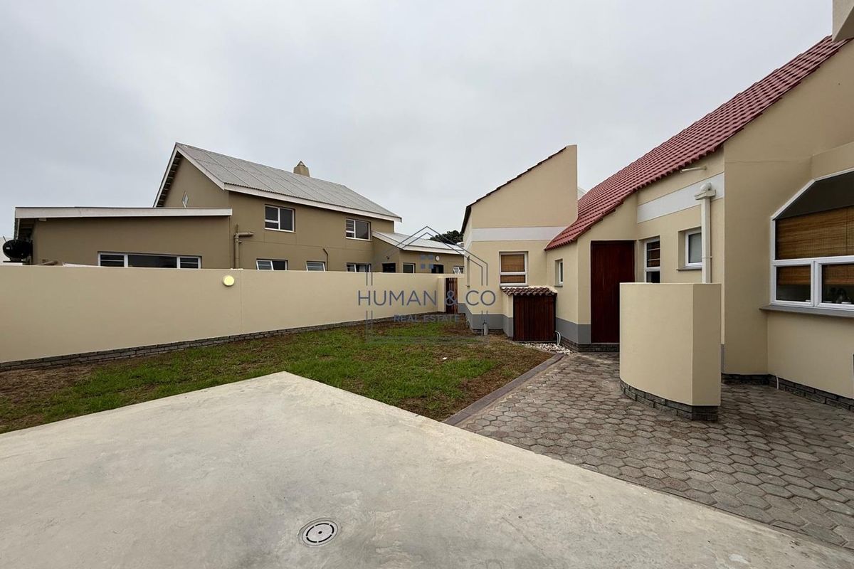 A rear exterior view of the property featuring a paved patio area, a small lawn, and perimeter boundary walls.