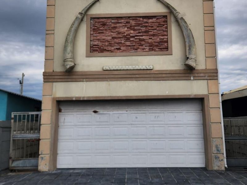 Front elevation of a garage featuring a white sectional door, stone cladding detail, and a paved driveway area.