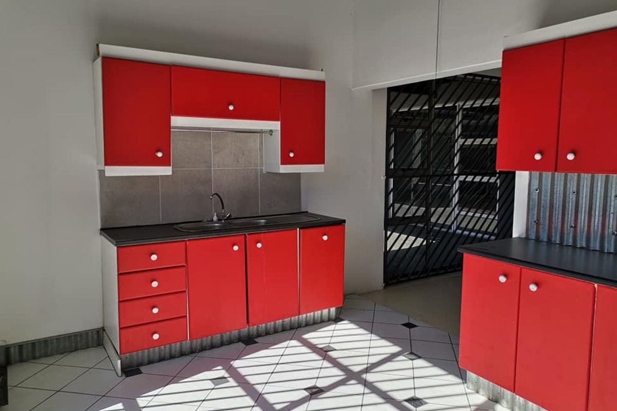 A functional kitchen area featuring bright red cabinetry, a stainless steel sink, and tiled flooring, leading to a secure gated entrance.