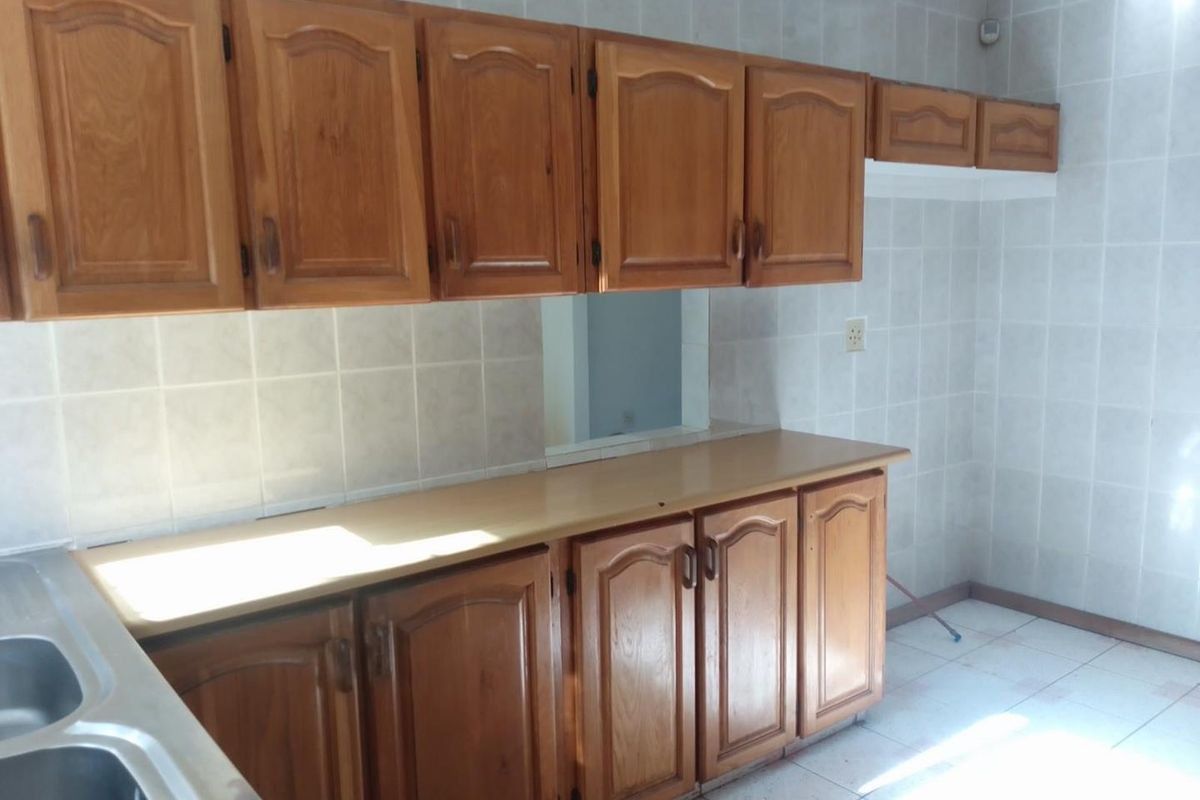 A functional kitchen featuring traditional wooden cabinetry, tiled splashbacks, and a stainless steel sink, offering a classic layout ready for modernization.