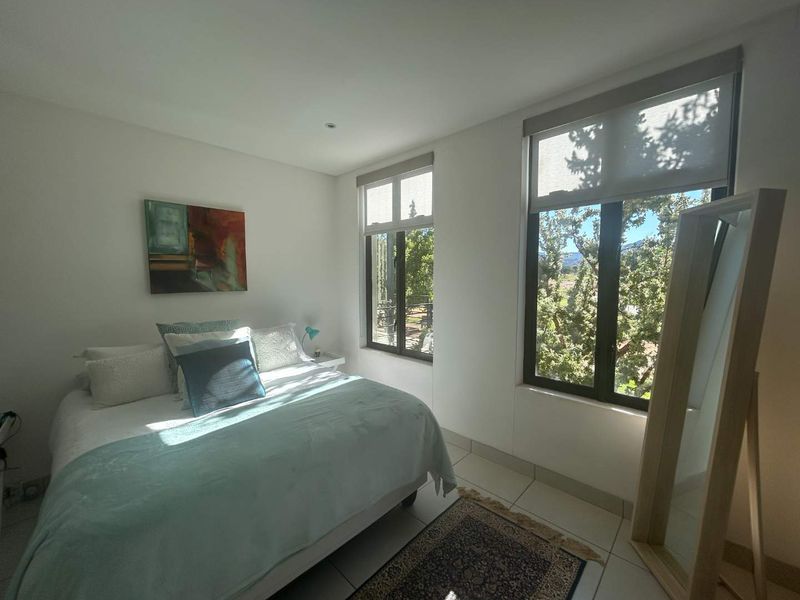 A bright and well-maintained bedroom featuring tiled flooring, recessed lighting, and large windows with roller blinds offering pleasant outdoor views.