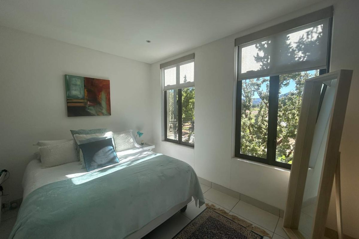 A bright and well-maintained bedroom featuring tiled flooring, recessed lighting, and large windows with roller blinds offering pleasant outdoor views.