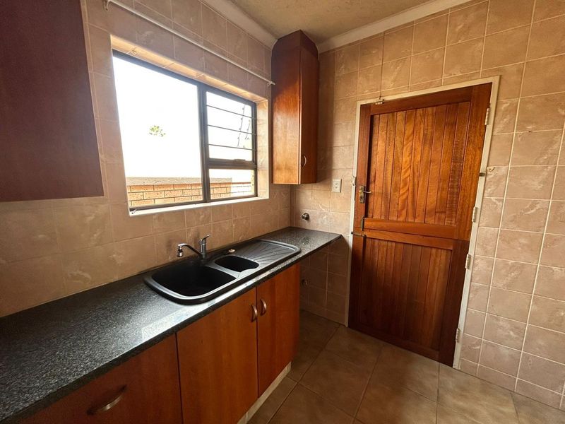 Functional scullery featuring granite countertops, double basin sink, wooden cabinetry, and a stable door leading to the exterior.
