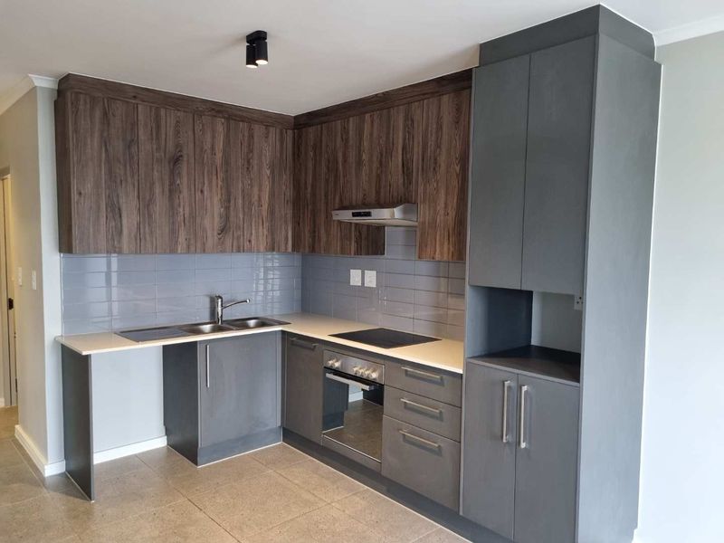Modern kitchen featuring dark grey and wood-grain cabinetry, stone countertops, integrated oven and hob, and a sleek tiled backsplash.