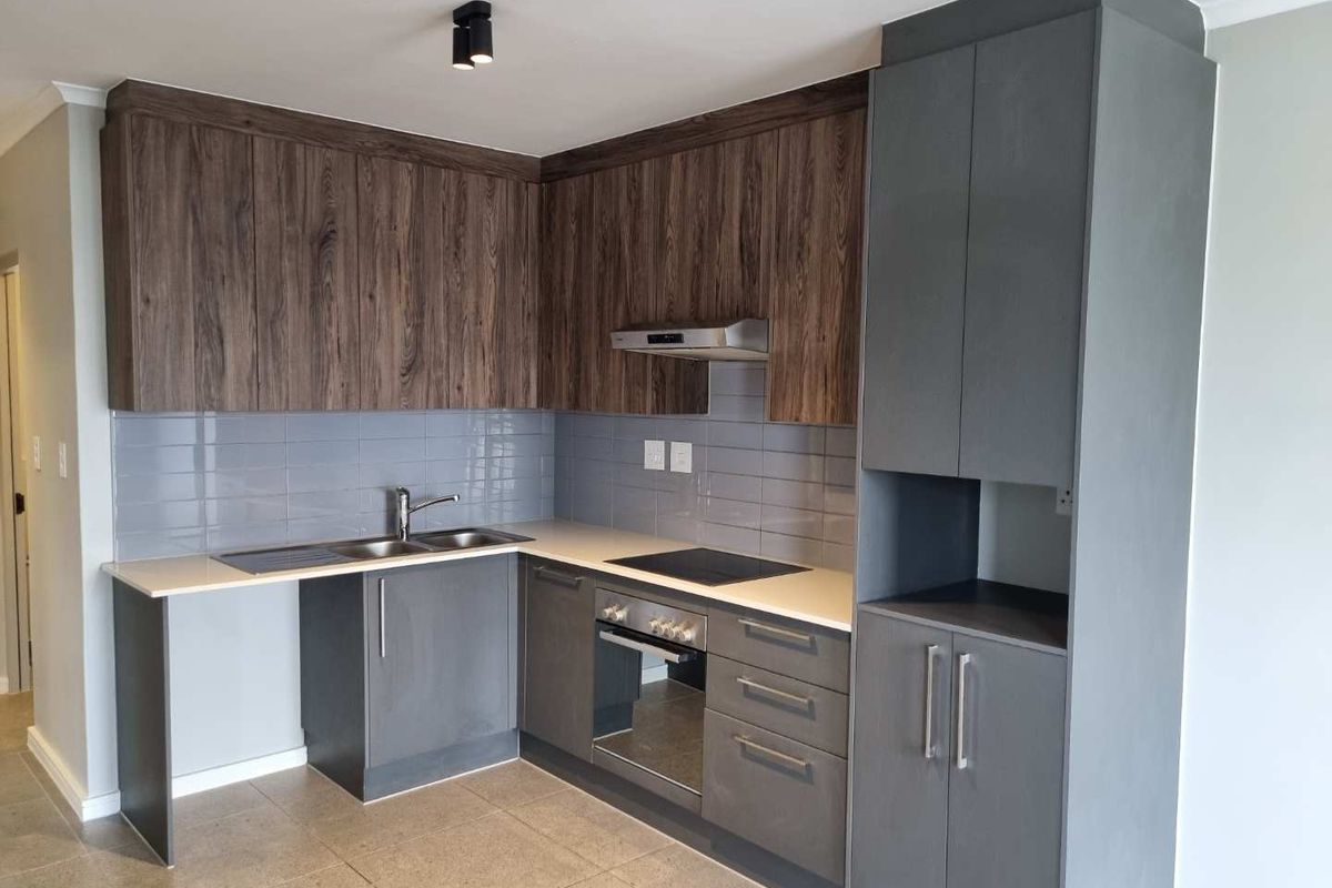 Modern kitchen featuring dark grey and wood-grain cabinetry, stone countertops, integrated oven and hob, and a sleek tiled backsplash.