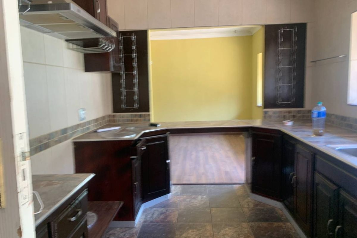 A functional kitchen featuring dark wood cabinetry, stone-look countertops, tiled flooring, and an integrated extractor fan, opening into an adjacent living space.