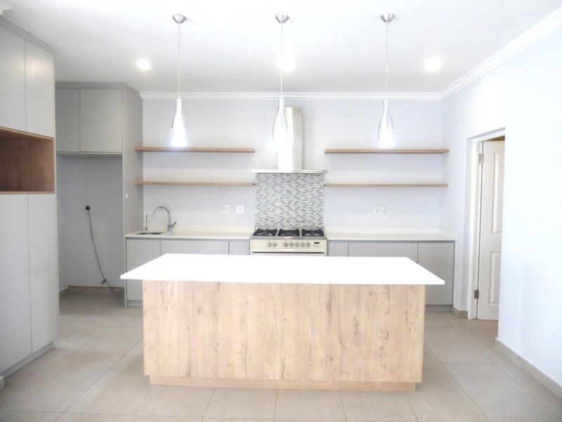Modern kitchen featuring a central island, gas stove with extractor, mosaic backsplash, floating shelves, and ample built-in cabinetry with neutral finishes.