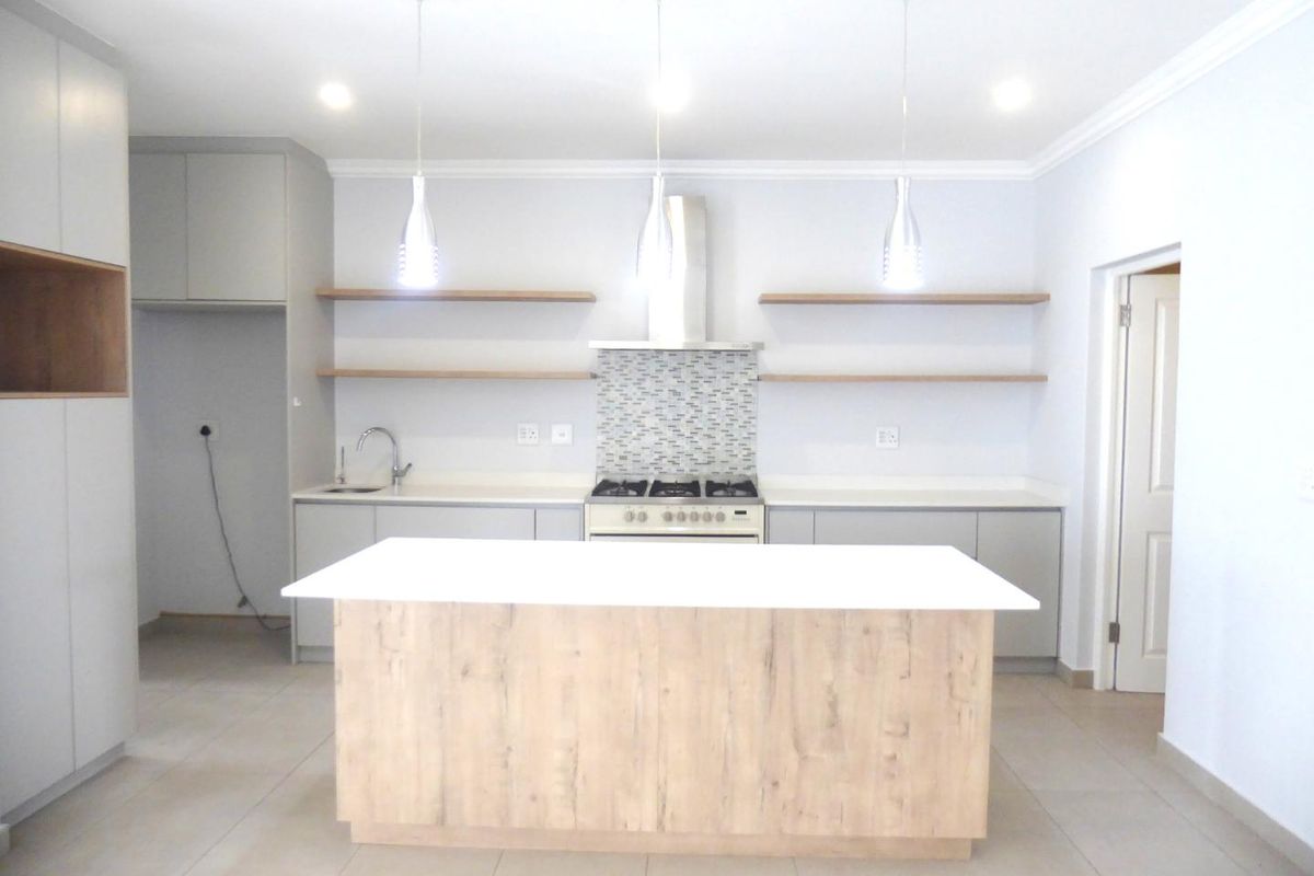 Modern kitchen featuring a central island, gas stove with extractor, mosaic backsplash, floating shelves, and ample built-in cabinetry with neutral finishes.